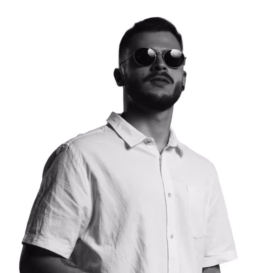 Portrait of a man wearing round sunglasses and a white button-up shirt, standing confidently with a slight upward gaze against a clean white background.